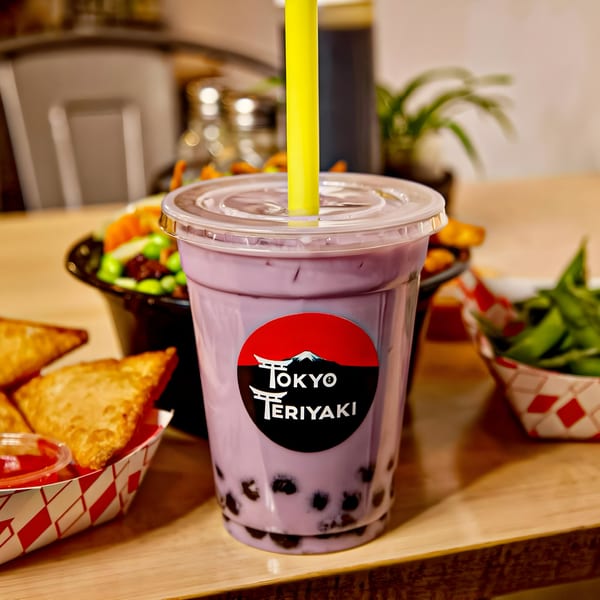 Tokyo Teriyaki taro bubble tea with a yellow straw, surrounded by appetizers on a wooden table.