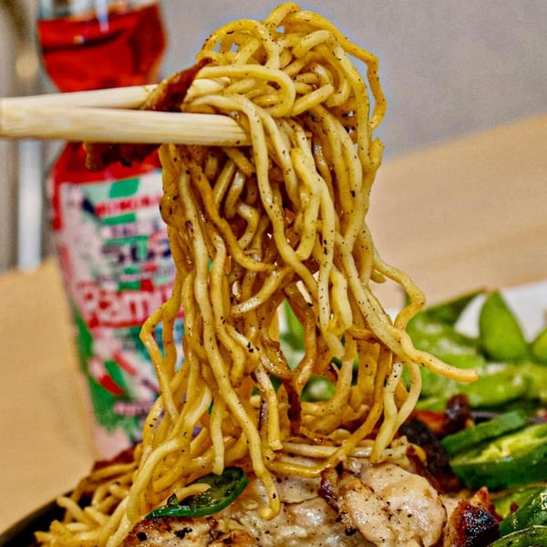 Chopsticks lifting a tangle of Tokyo Teriyaki noodles with chicken and green peppers below.